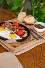 English breakfast. Fried eggs with fried sausages, bacon, tomatoes and mushrooms. On a wooden with bean paste.