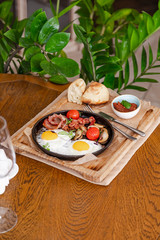 English breakfast. Fried eggs with fried sausages, bacon, tomatoes and mushrooms. On a wooden with bean paste.