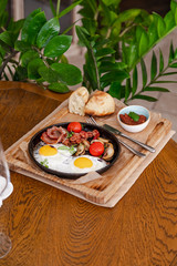 English breakfast. Fried eggs with fried sausages, bacon, tomatoes and mushrooms. On a wooden with bean paste.