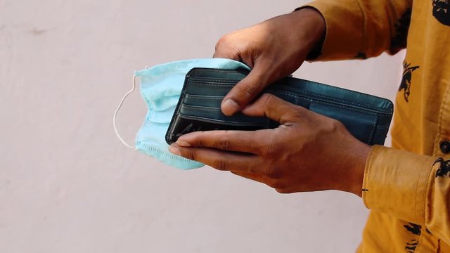 Closeup shot of hands of an Indian man holding an empty wallet and medical face mask during the corona virus Pandemic