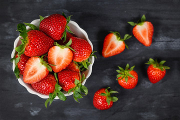 Top view of strawberries in a bowl showing fresh ripe whole and cut in half strawberry fruits in a white bowl on dark background