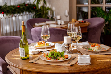 Served table with dishes. On the table are shrimp salad, olivier salad, mashed potatoes with meatballs and an English breakfast. White wine is served for the meal.