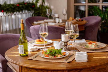 Served table with dishes. On the table are shrimp salad, olivier salad, mashed potatoes with meatballs and an English breakfast. White wine is served for the meal.