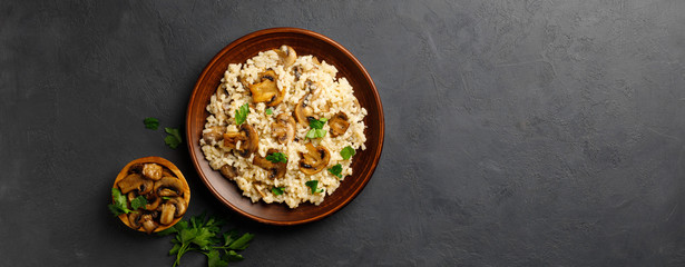 A dish of Italian cuisine - risotto from rice and mushrooms in a brown plate on a black slate background. Top view. Flat lay. Copy space.