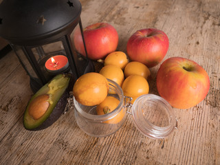 Red apples, medlars and avocado next to a lit lantern.