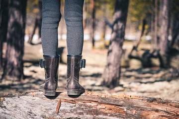 The girls thin legs in rubber boots cross the forest through fallen tree on camping trip.