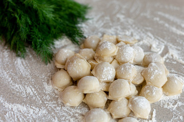 Fototapeta na wymiar Homemade dumplings close-up. Dumplings lie on a table sprinkled with flour and next to dill greens. A lot of dumplings in bulk