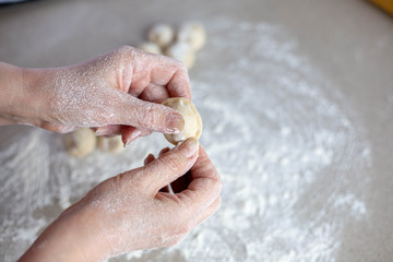 Fototapeta premium Woman sculpts homemade dumplings bear ears in the kitchen. Modeling dumplings closeup. Female hands sculpt dumplings.