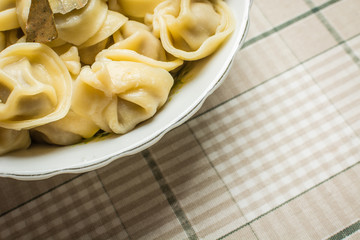 Handmade boiled shaped dumplings with bay leaves in large plate on kitchen table.