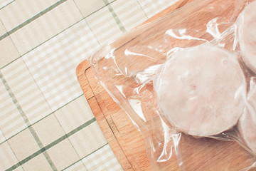 Frozen hake fish fillet in sealed package on wooden cutting board.