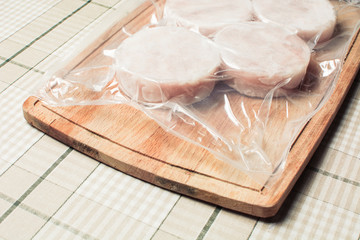 Frozen hake fish fillet in sealed package on wooden cutting board.