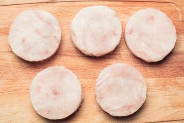 Chunks of frozen fish fillet hake on wooden cutting board.
