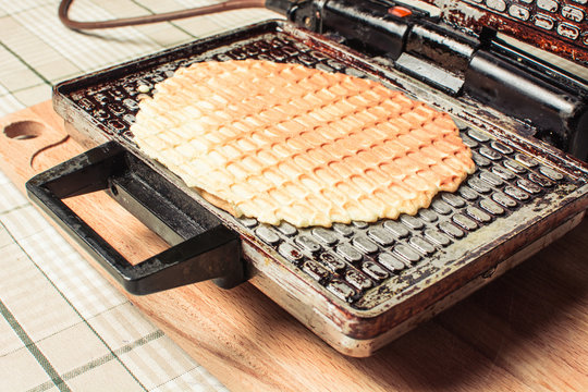 Thin waffles are roasted in waffle iron on kitchen table.