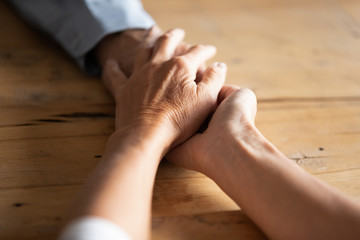 Compassionate middle aged wife covering wrinkled hand of retired husband, overcoming grief together. Elderly woman giving psychological support to mature man or having sincere conversation indoors.