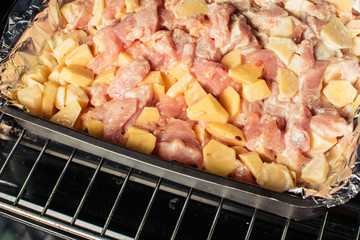 Pickled pieces of chicken fillet with potatoes in baking tray in oven.