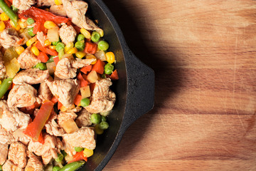 Fried tender chicken pieces with vegetable mixture in pan on wooden board.