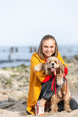 Young woman in a yellow coat hugging a dog at the sea shore.