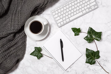 Cozy home office workspace. Marble desk with warm wool plaid, green ivy leaves, coffee cup,...