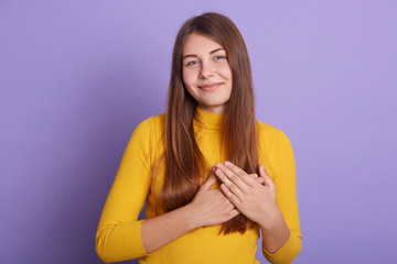 Pretty woman with closed eyes, keeps hands on chest, expresses her sympathy to someone, being...