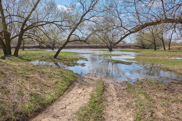 Spring landscape with a flooded dirt road by the river