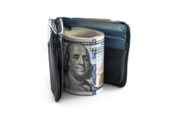 Close up of a black leather bi-fold wallet standing on edge with a wad of cash including hundred dollar bills rolled up between the open wallet with white background copy space.