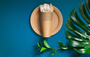 Eco friendly craft paper tableware on blue background with monstera leaf. Recycling concept.