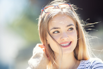 Beautiful young blonde girl wearing dental braces, smiling and looking to the side