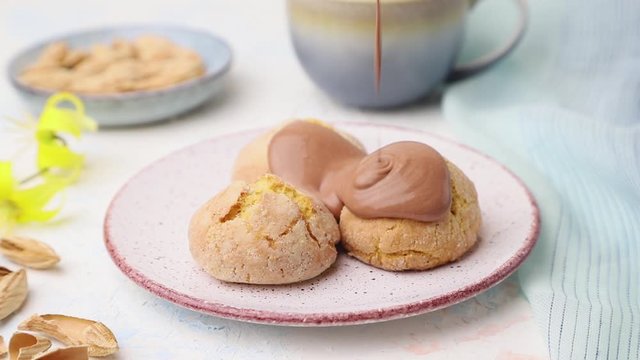 almond cookies poured with chocolate sauce on ceramic plate on a white background with blue textile. Side view, close up.