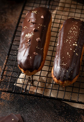 close-up of profiteroles topped with chocolate glaze and golden powder (kandurin). gourmet dessert. dark background. vertical image.