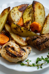 Macro view of fried potatoes with carrot and grilled meat slices on a white plate