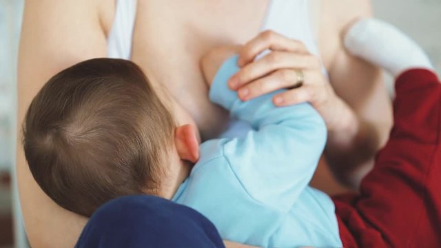 A Mother breastfeeding her little baby in her arms. close up mom nursing and feeding small kid. Child hurt bites the nipple on mother breast.