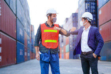 Technician or engineer workers with face mask show new style of greeting together in shipping container workplace area. Concept of procedure to prevent virus infection in for member in company.