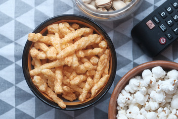 Close up of bowl of popcorn, chips and tv remote on wooden background 