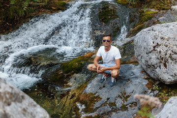 young man sitting on rocks in the river