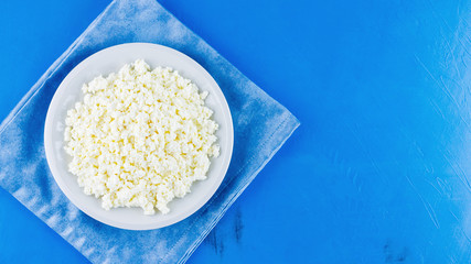 Cottage cheese in a white plate on a blue background. Organic eco healthy meal, dairy product. Plate of cottage cheese on a blue napkin. Top view. Copy space