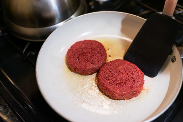 Closeup of two raw vegan meat sausage patties cooking on ceramic nonstick frying pan with oil grease spatula flipping
