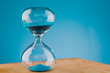 Close-up of an hourglass clock on a light blue background on a wooden table.