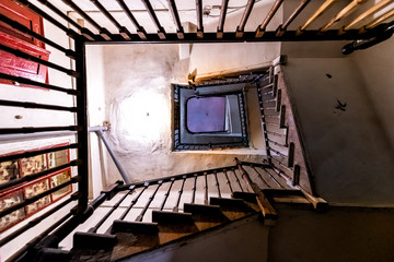 Looking up low angle abstract view of old dark stairway staircase in run-down apartment building in...