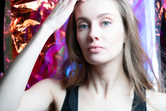 Portrait of a beautiful model girl in the studio, on the background shiny foil shimmering in different colors