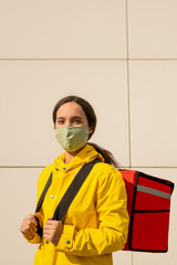 Young brunette female in yellow jacket and mask delivering orders to clients