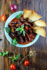 Mussels in tomato sauce with garlic in a blue plate on a brown wooden background