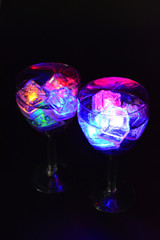 Large glasses with different colors of luminous ice cubes with a tasty drink are located on a black matte background.