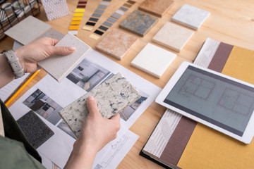 Hands of young female designer holding two samples of marble tile over table - obrazy, fototapety, plakaty