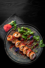 sushi rolls with bacon and chicken in plate on black wooden table background