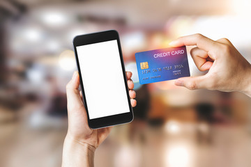 Hands holding credit card with Smart mobile phone show white background for product mockup over for online shopping on shopping mall background, E-payment technology, Concept of internet banking