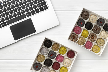 Two boxes of vegan sweets energy balls near the laptop on white wooden table