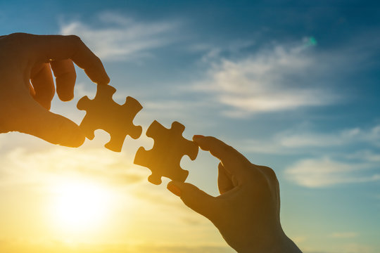 Two hands of businessmen connect the puzzle into a single unit against the backdrop of the sunset. Business concept idea, partnership, cooperation, teamwork, innovation