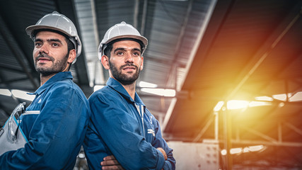 Confident engineers in blue jumpsuits looking ahead in the warehouse.	
