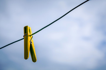 yellow clothespin hanging on a rope against a cloudy sky
