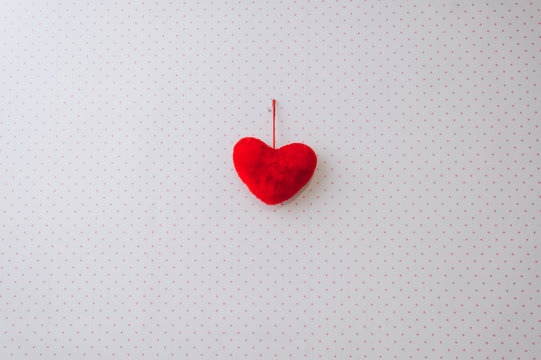 Red woolen heart hanging on a nail against the background of a multi-colored wall as a decoration. Photography, concept.